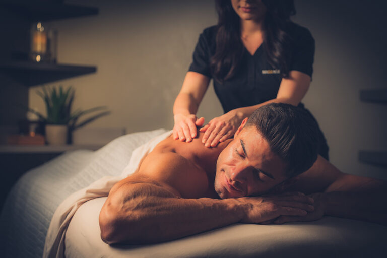 Skilled Asian therapist performing traditional Thai massage on a male client in loose spa attire in a warm candlelit boutique spa